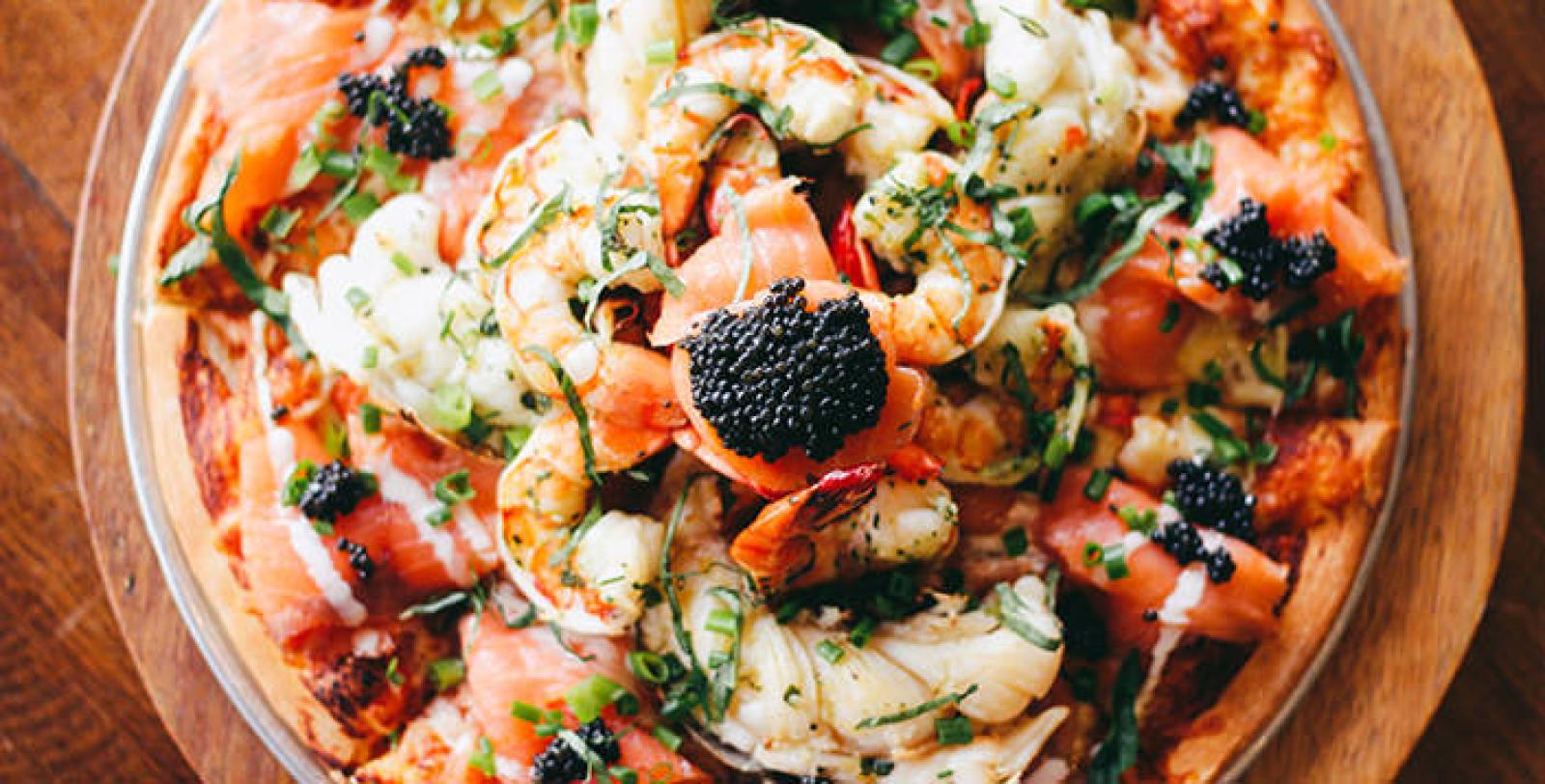 Seafood pizza topped with prawns, melted cheese, herbs and a black olive on a wooden board