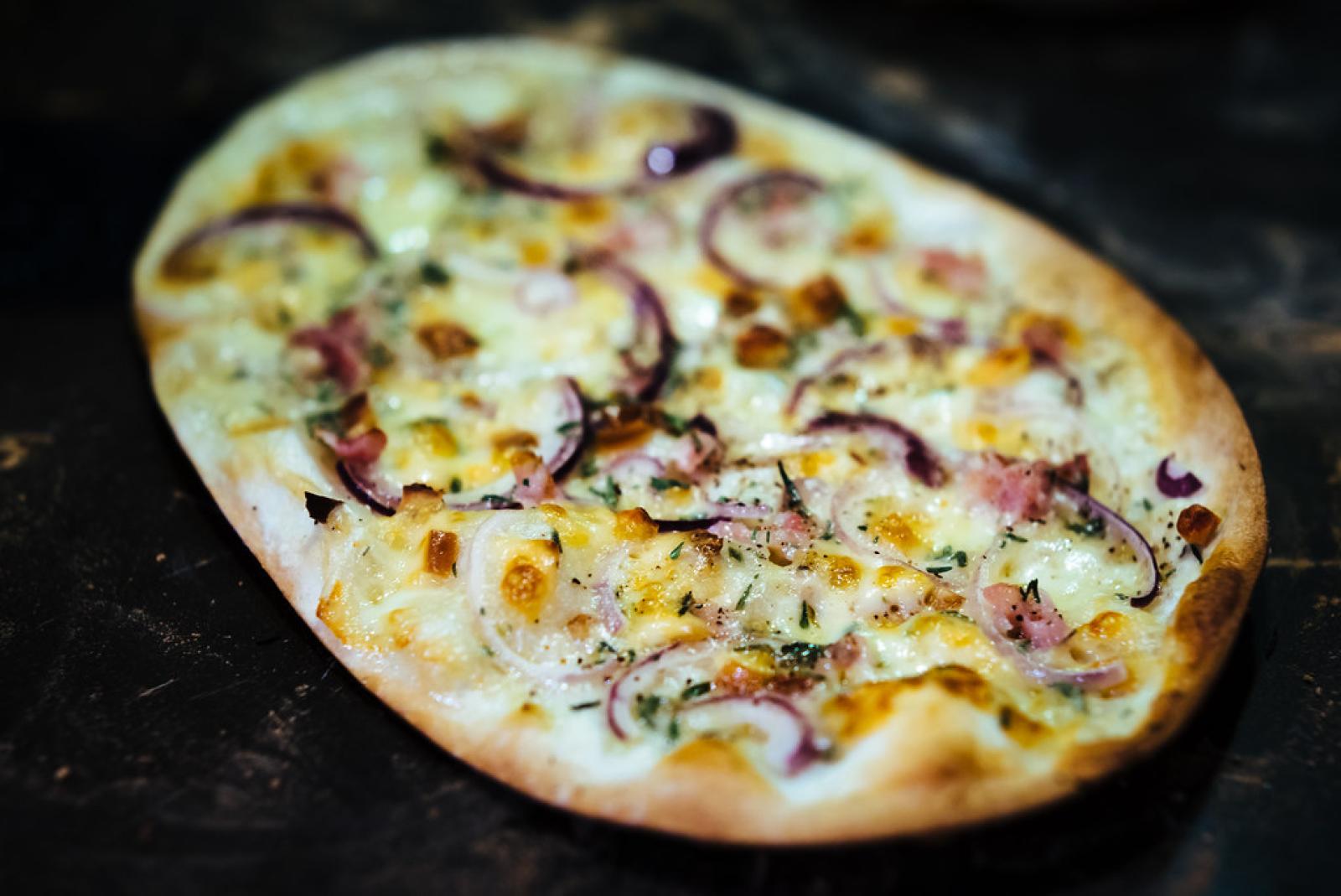 Oval Lebanese flatbread topped with melted cheese, red onion and herbs on a dark surface
