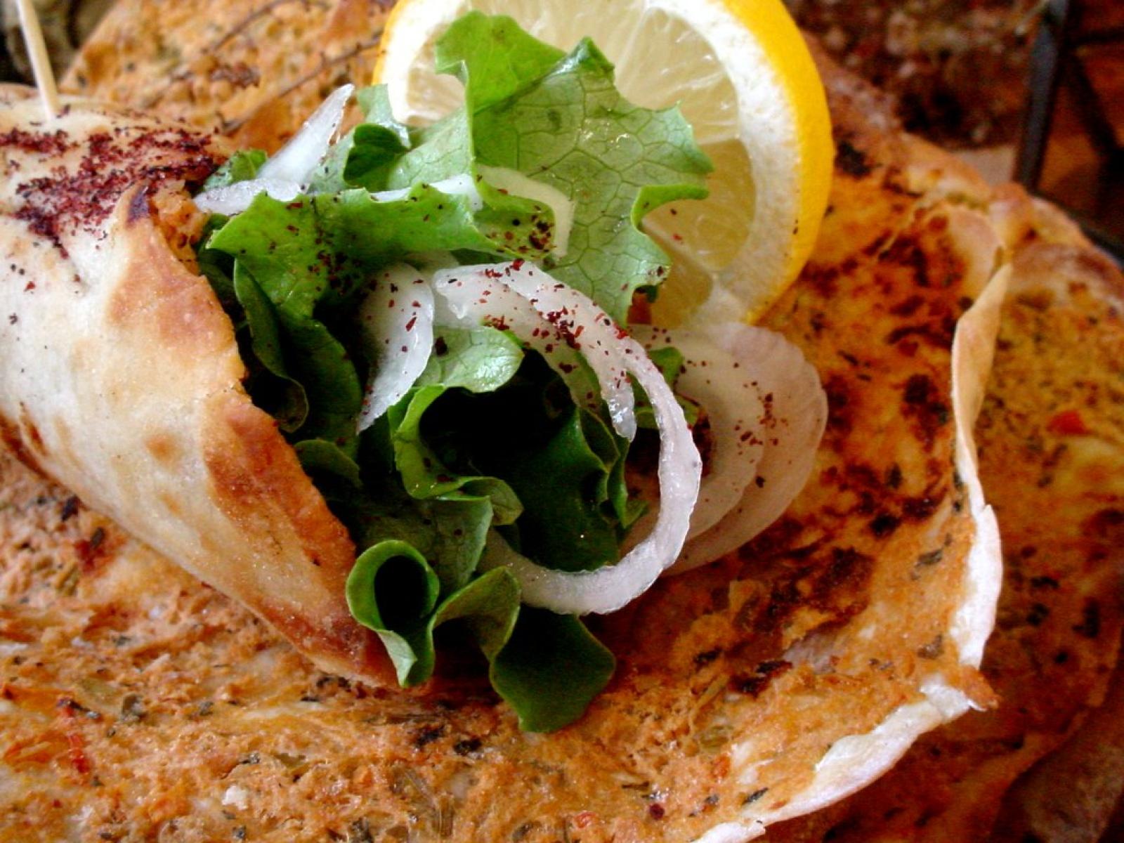 Close-up of a Lebanese wrap with leafy greens, onion, lemon and creamy sauce on toasted flatbread