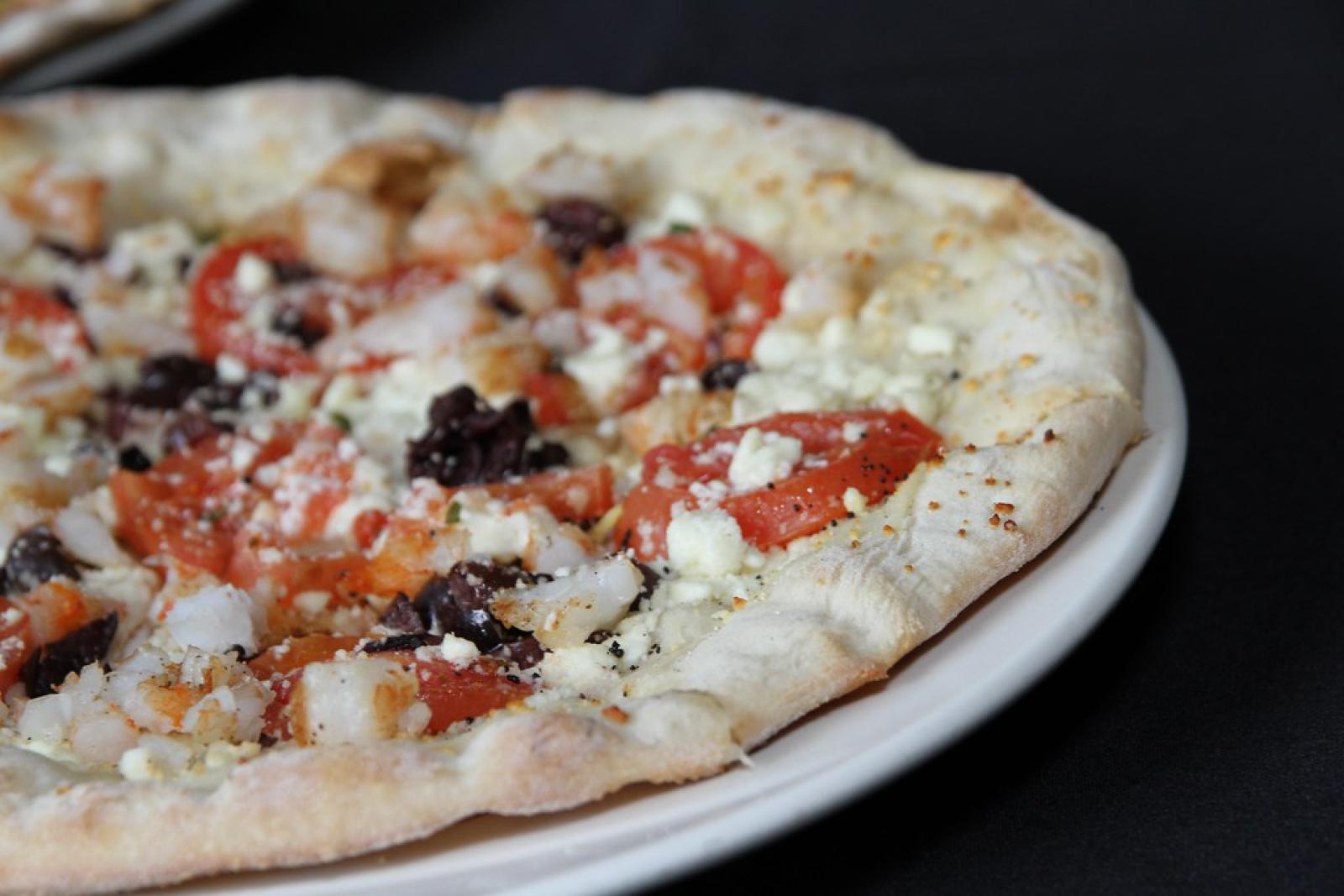 Close-up of a freshly baked Lebanese-style pizza with cheese, tomatoes and black olives on a white plate