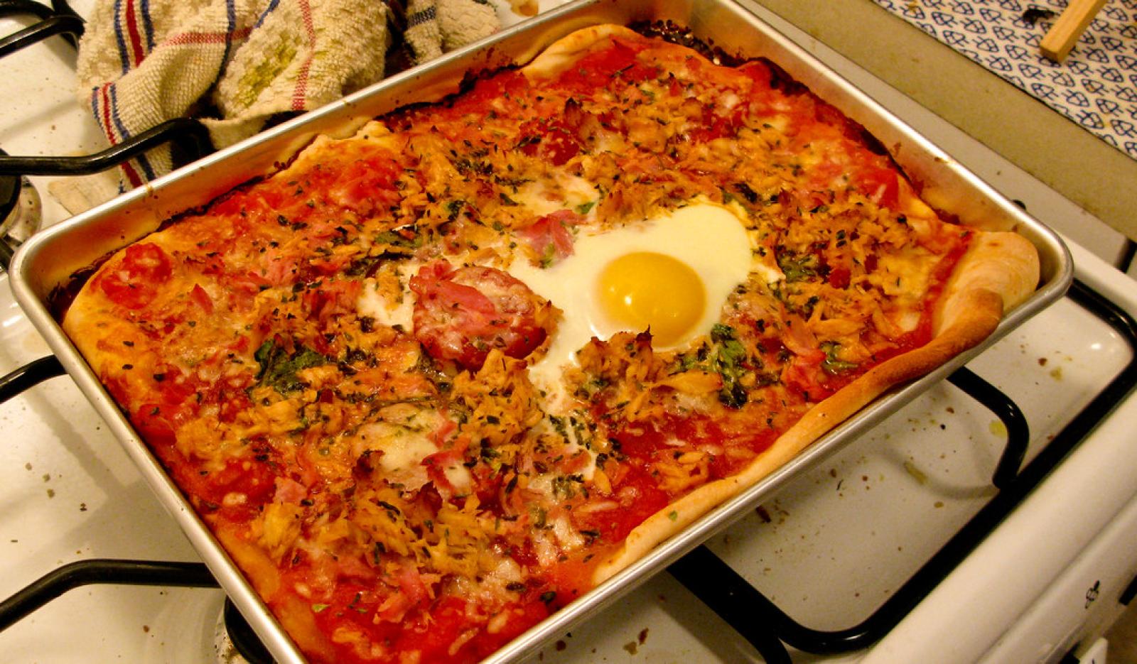 Rectangular baked pizza topped with tomato, cheese, herbs and a sunny-side-up egg