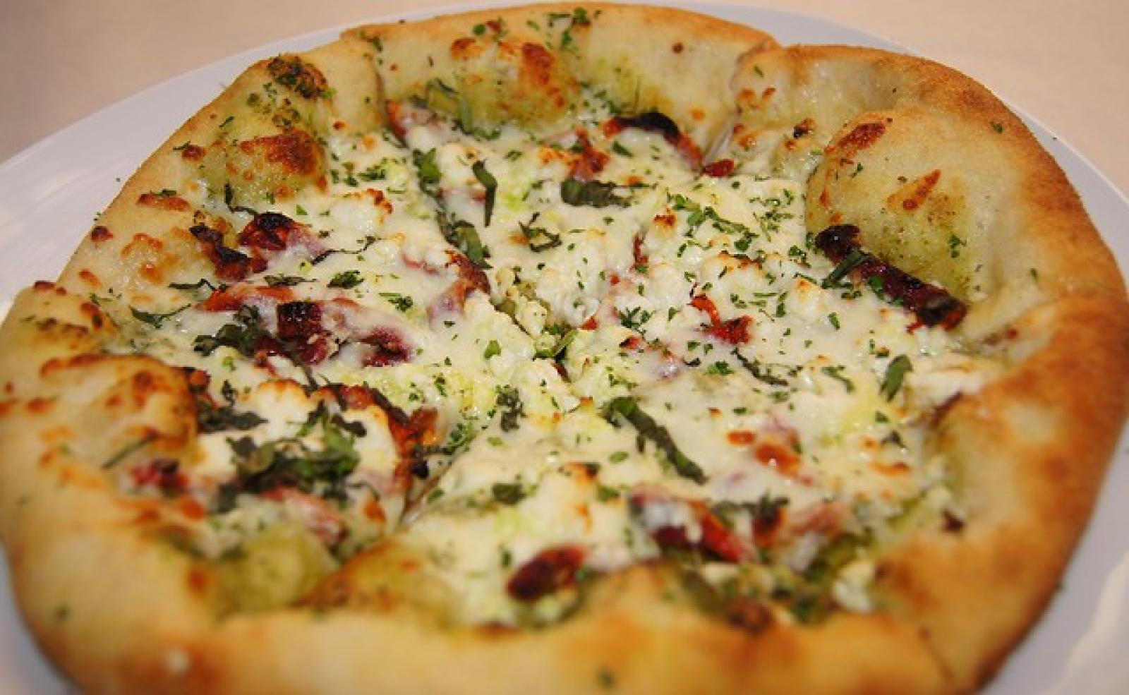 Close-up of a Lebanese-style cheese flatbread topped with herbs, spinach and sun-dried tomatoes
