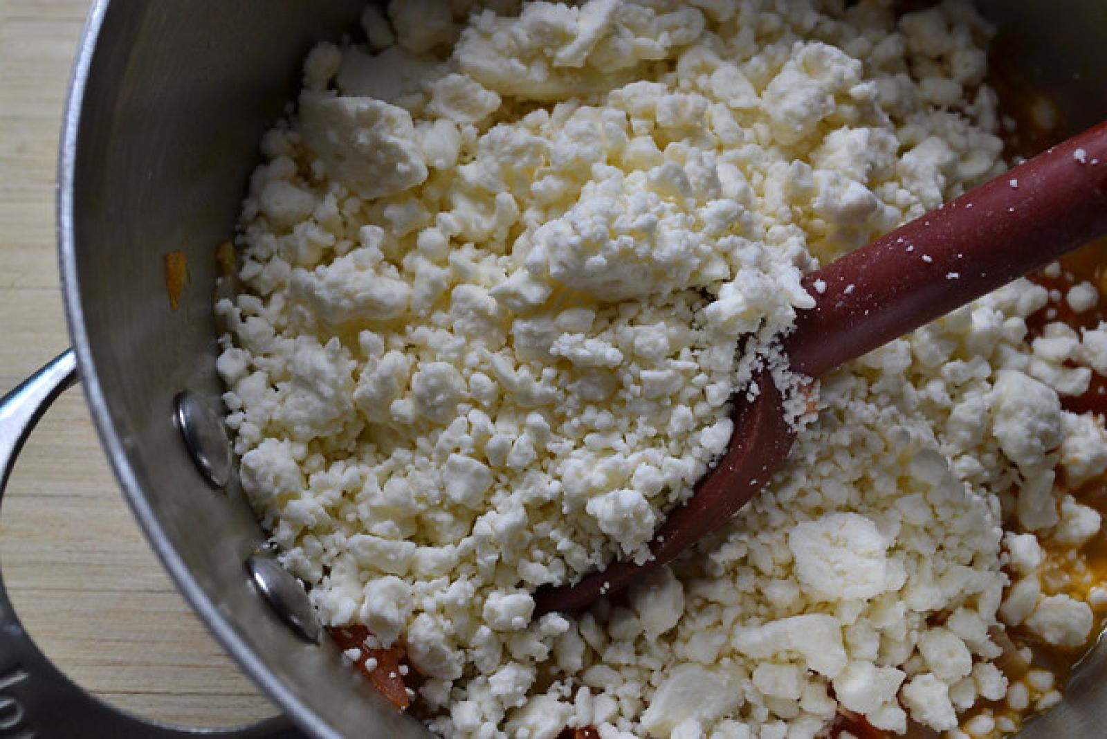 Wooden spoon stirring crumbled white cheese in a stainless-steel bowl
