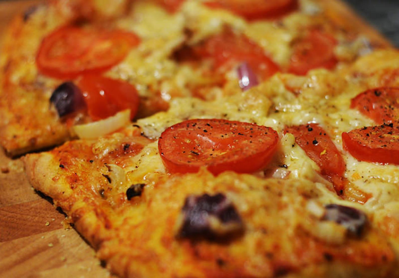 Close-up of sliced cheese pizza topped with cherry tomatoes, black olives and herbs