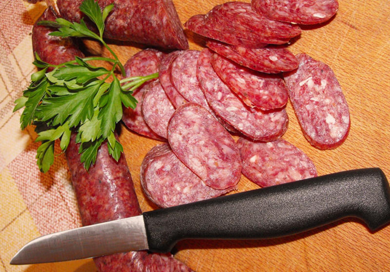 Sliced cured sausage with parsley and a kitchen knife on a wooden board