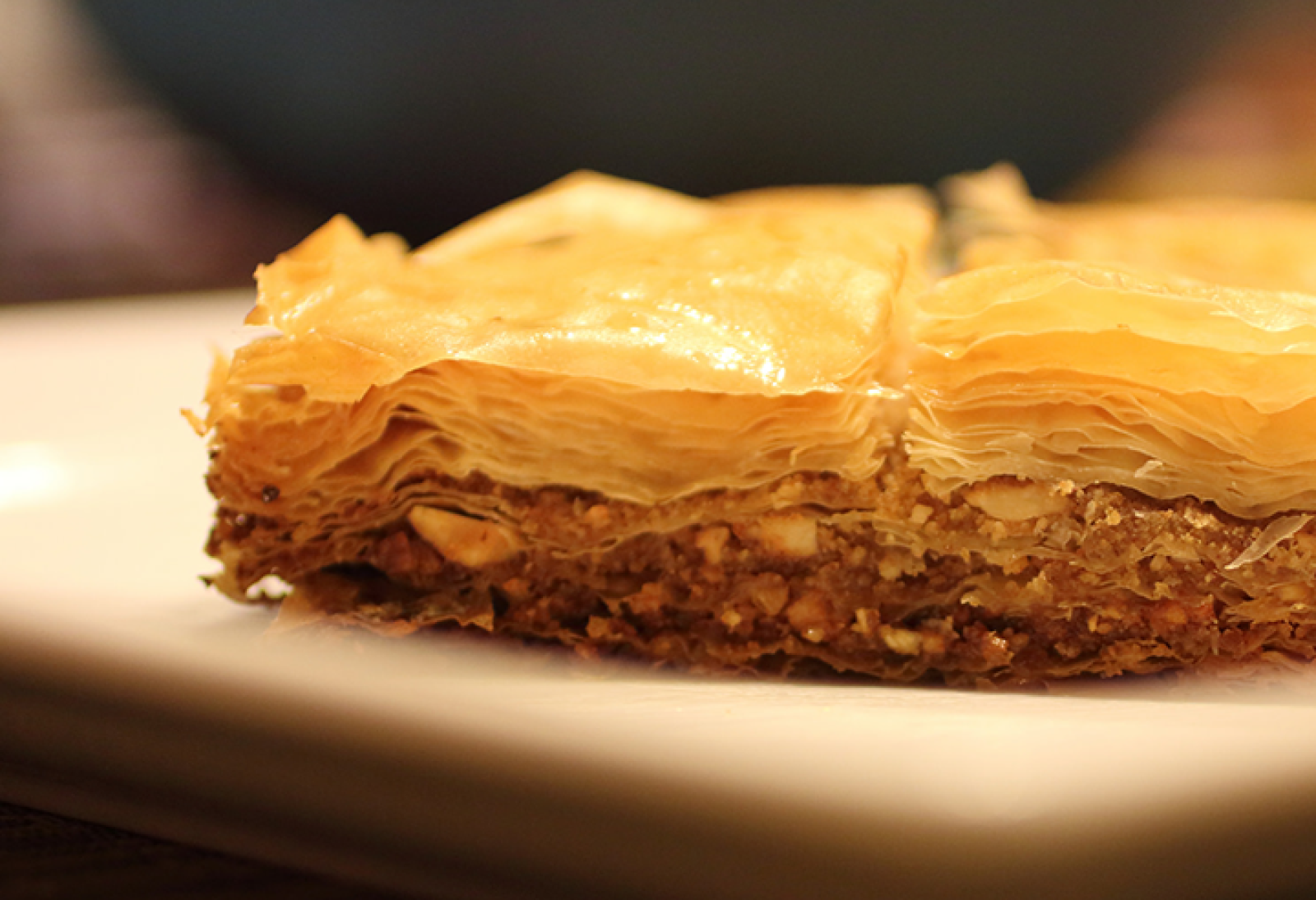 Close-up of a slice of golden baklava with crisp filo pastry and a nut filling on a white plate