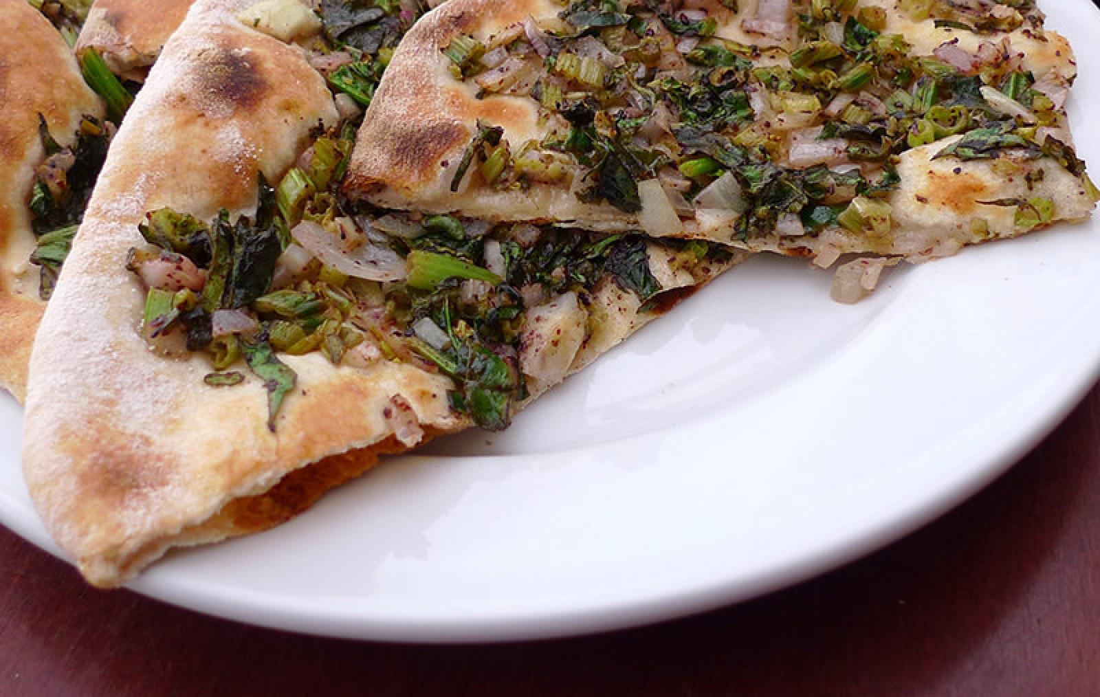 Slices of Lebanese zaatar flatbread topped with herbs and vegetables on a white plate