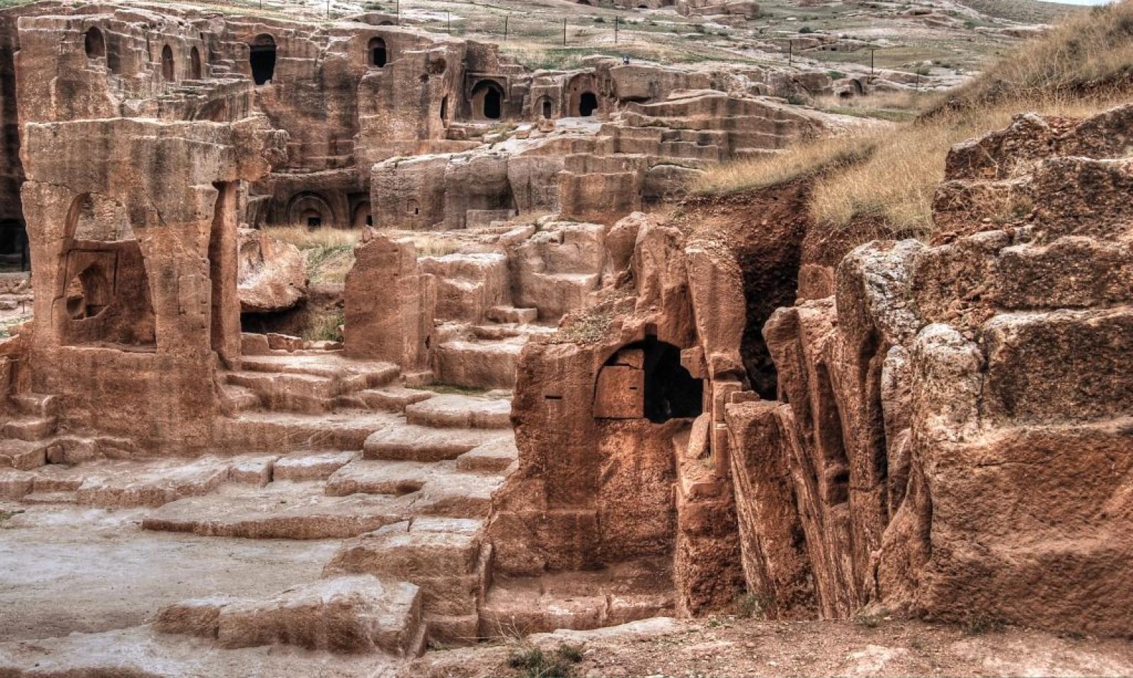 Ancient rock-cut stone ruins and carved chambers in a dry Middle Eastern landscape