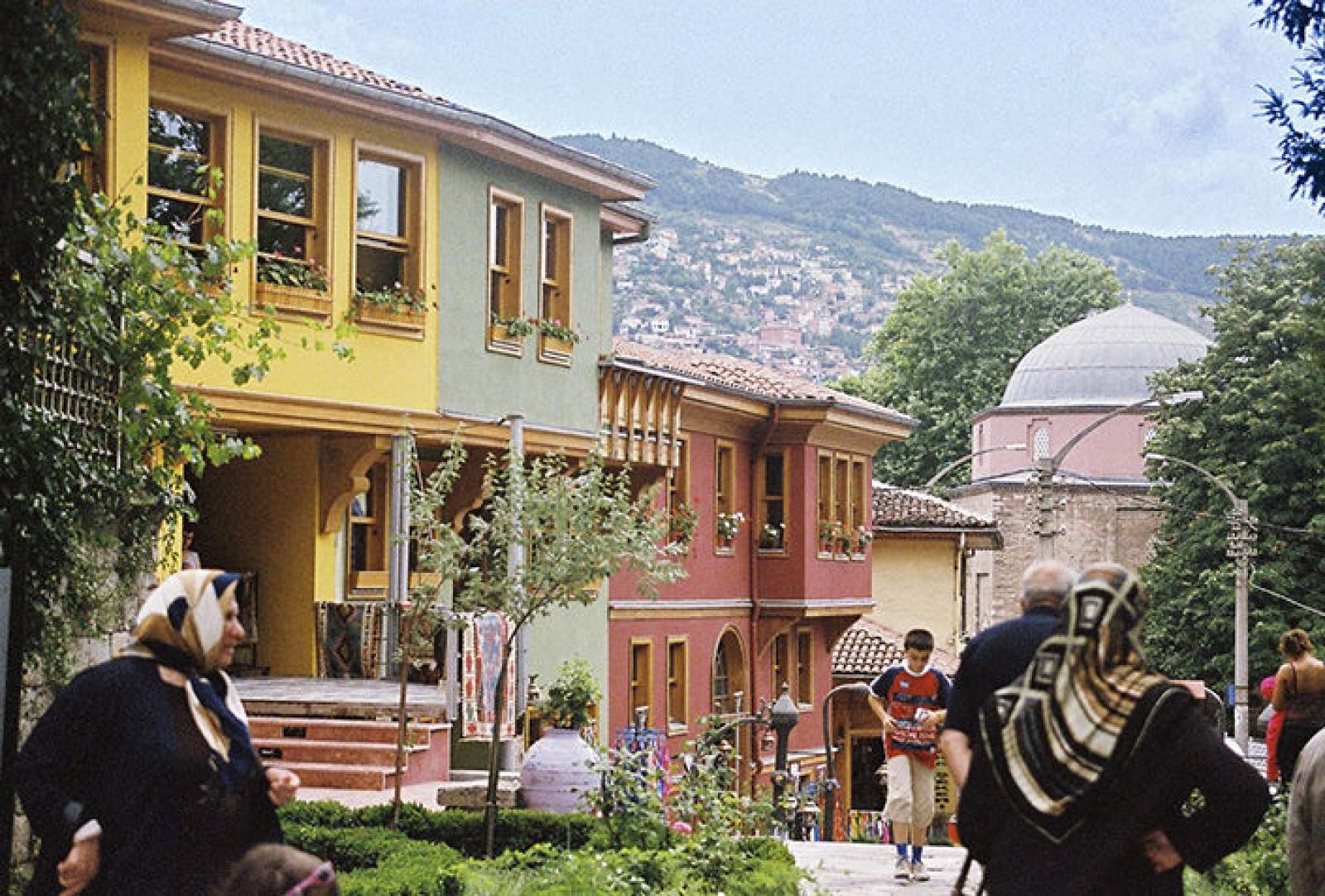 Pedestrians in a colourful hillside Middle Eastern neighbourhood with a mosque dome