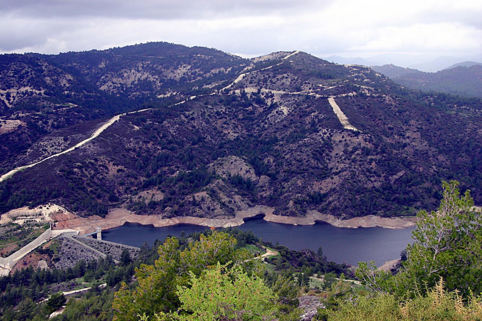 Mountain reservoir surrounded by rugged hills and green shrubs beneath a cloudy sky