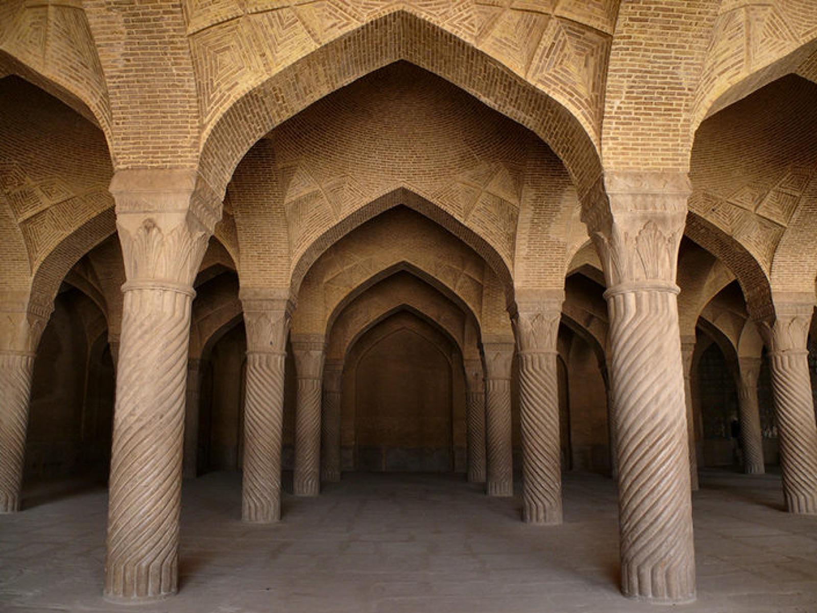 Rows of carved stone columns and pointed brick arches in a historic Persian interior