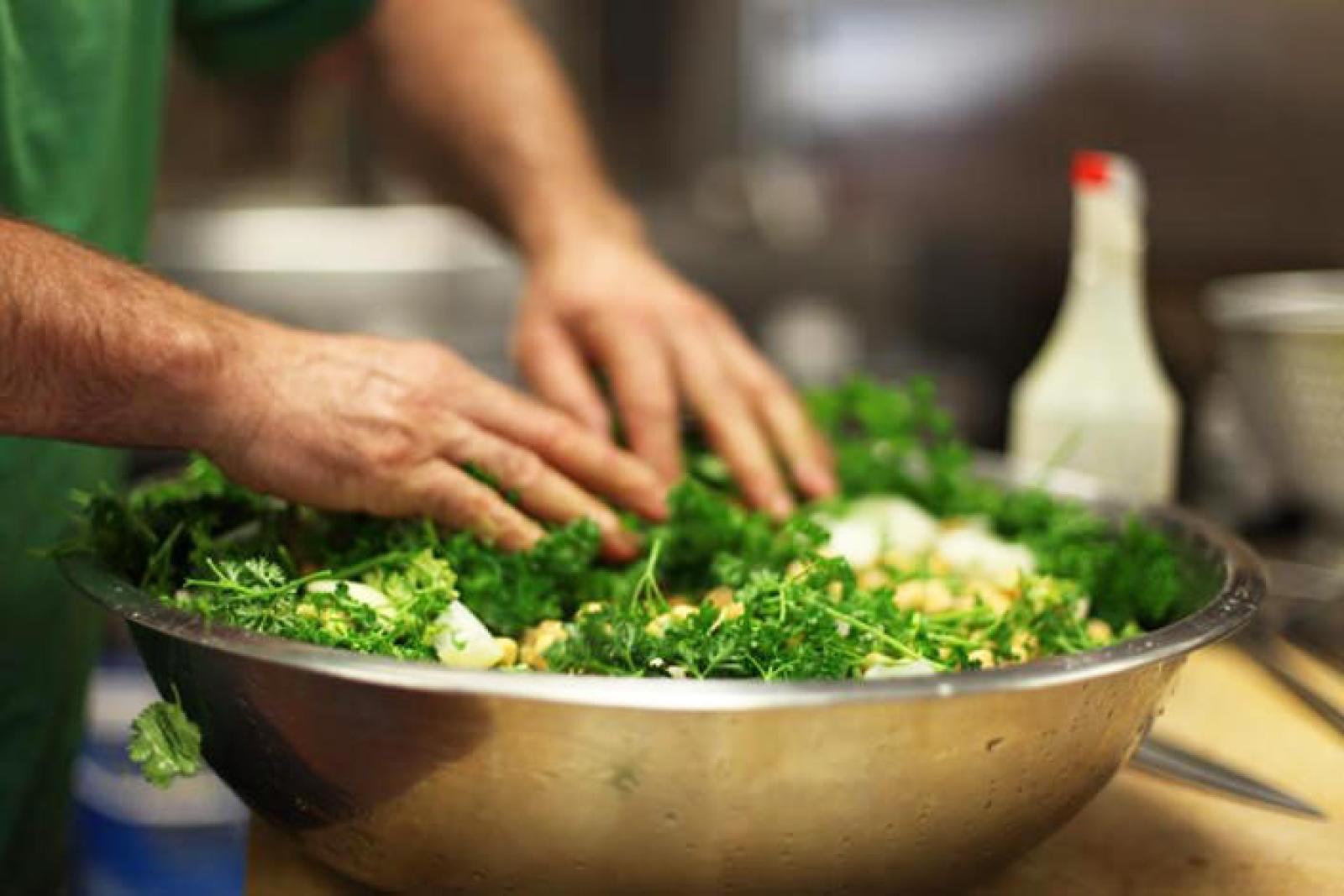 Chef mixing a fresh green herb salad in a large stainless steel bowl