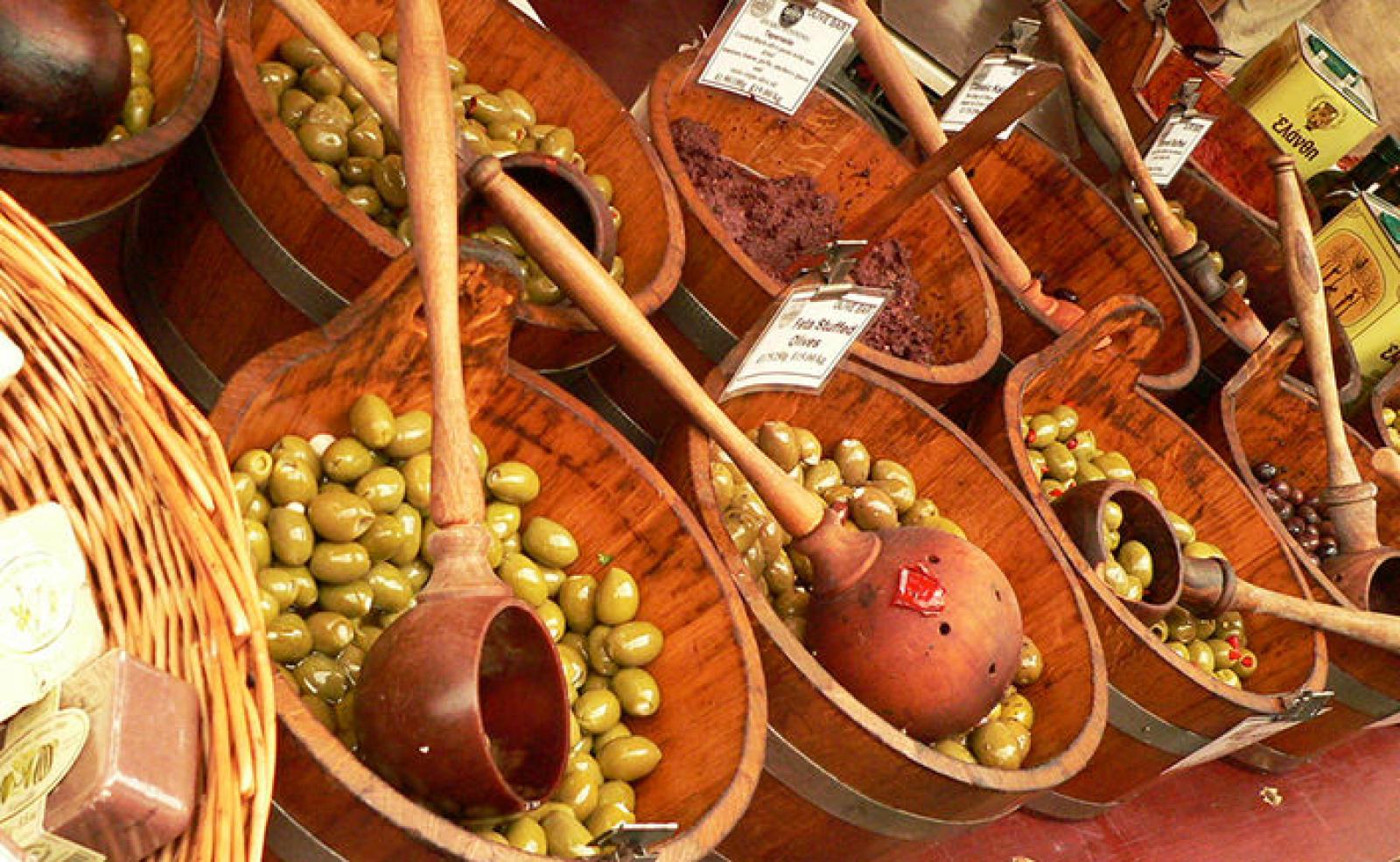 Wooden bowls of green olives, dried spices and scoops at a Mediterranean market stall