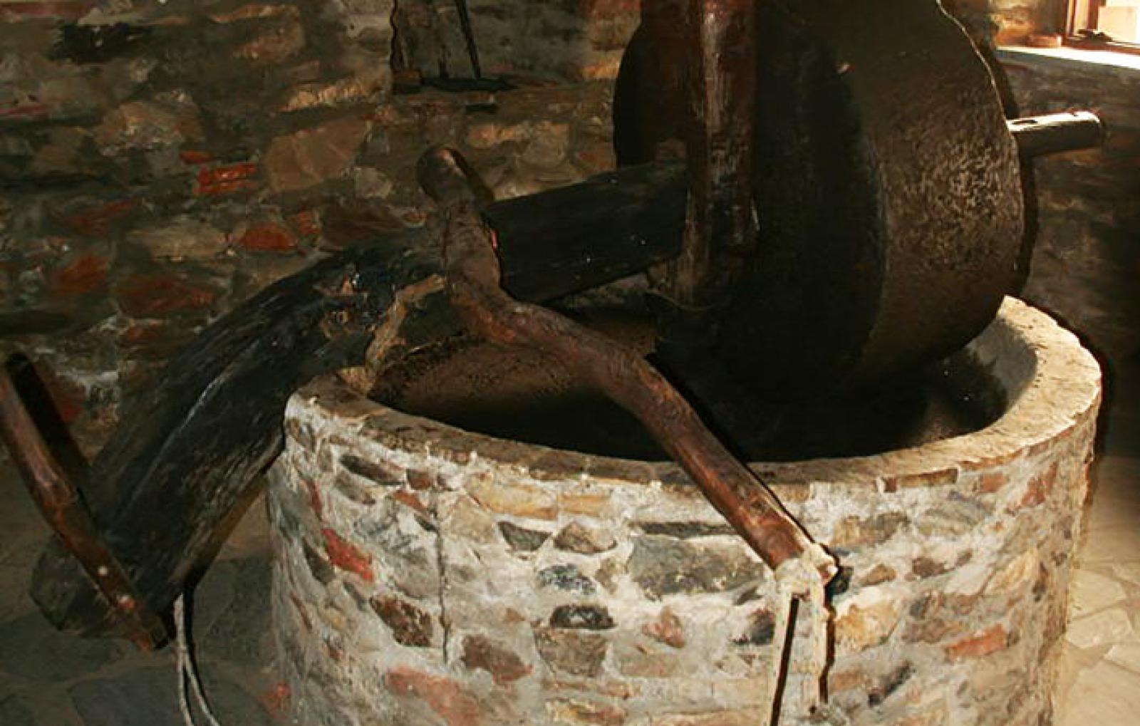 Traditional stone olive oil press with a large grinding wheel and wooden handles