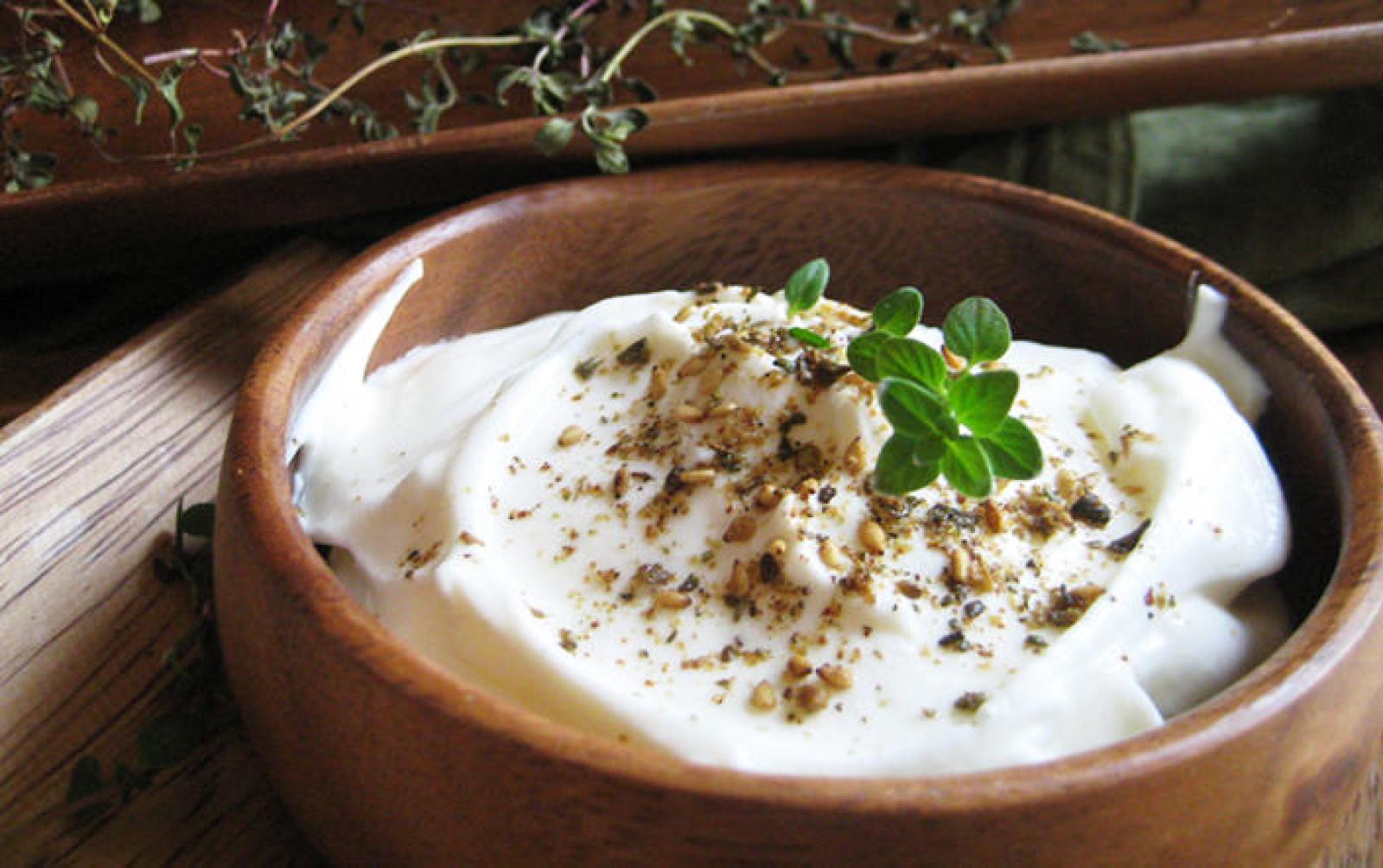 Bowl of creamy labneh topped with dried herbs and a fresh green sprig